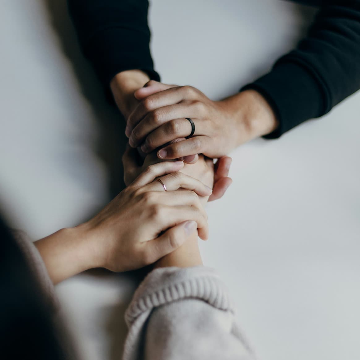 Two pairs of hands clasped together on a pale table top, seen from above.