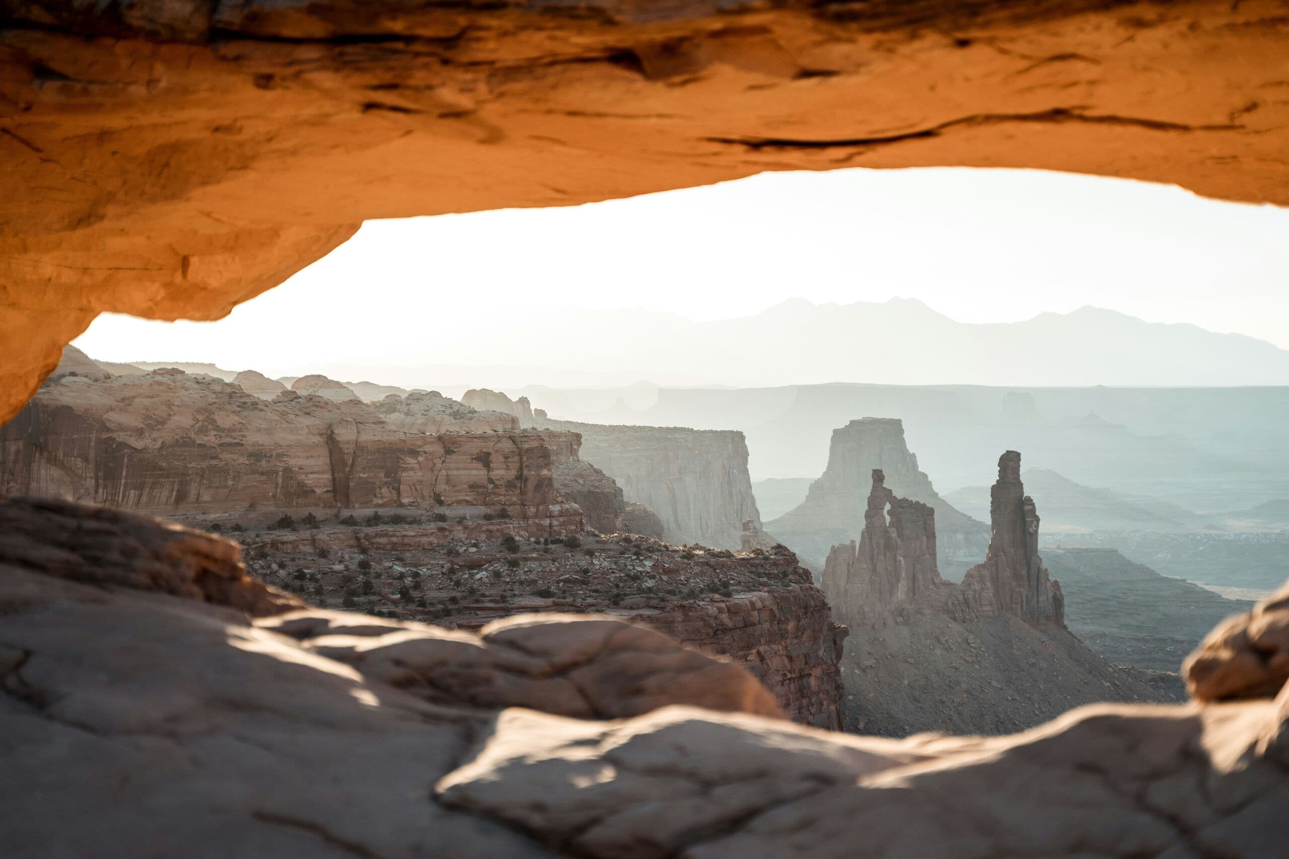 A canyon landscape seen through a sandstone arch in early morning light.